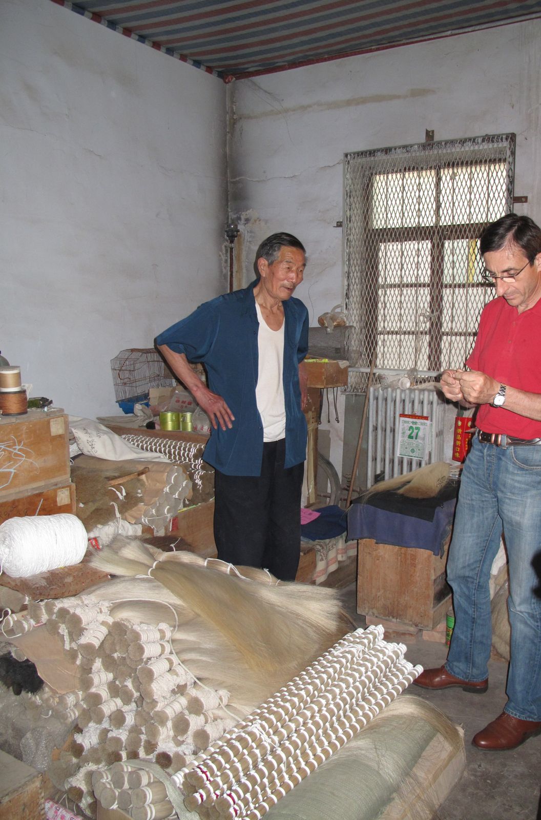 Bundles of raw horsehair stacked in a storeroom, with two men examining a sample